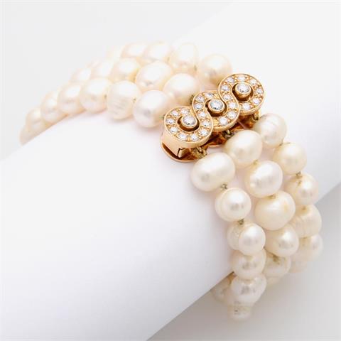 Dreireihiges Perlarmband mit einem länglichen, rundlich verschlungenen Verschluss besetzt mit weißen Steinen.
